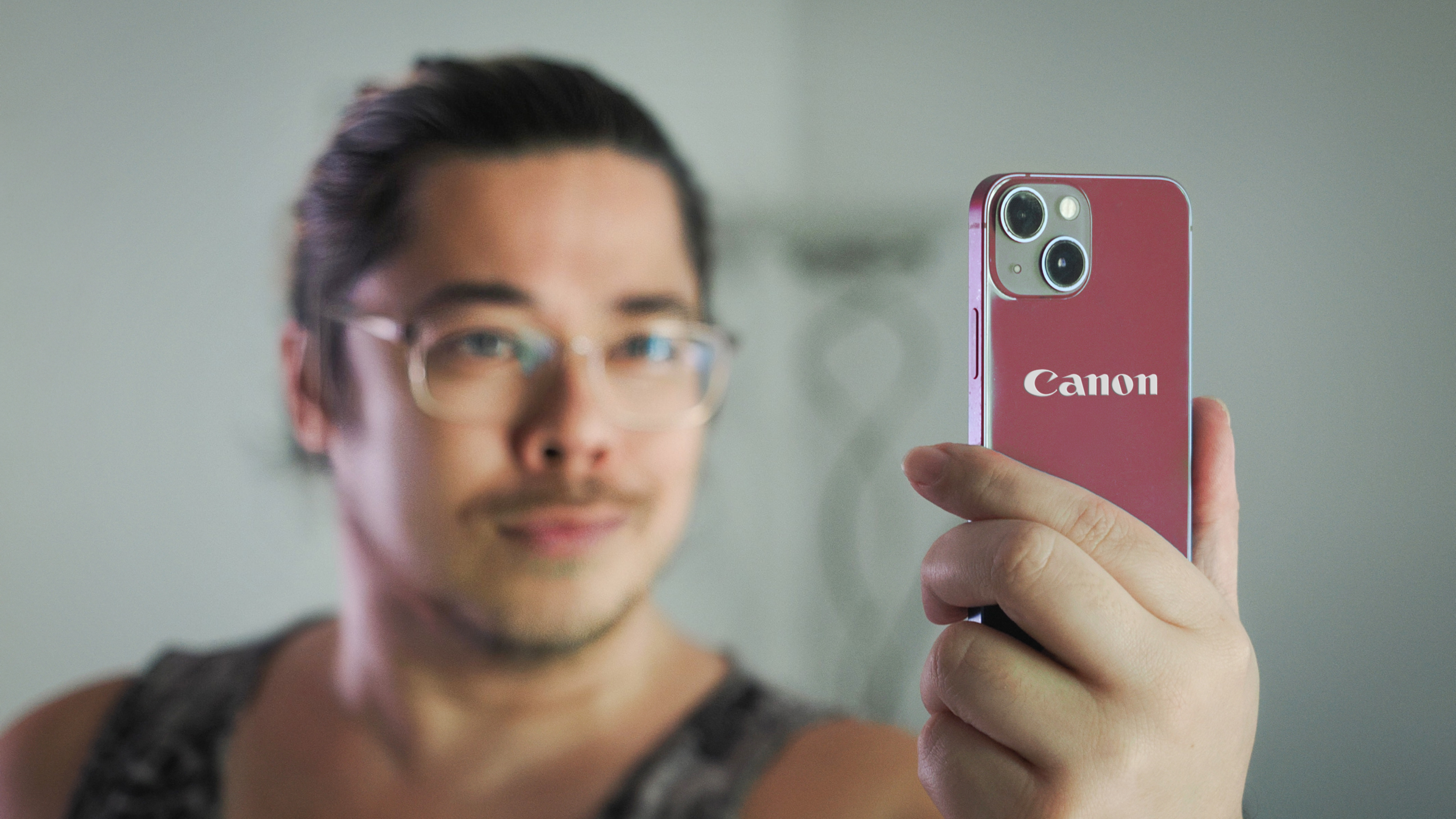 Man holding up a red smartphone with a Canon logo on the back 