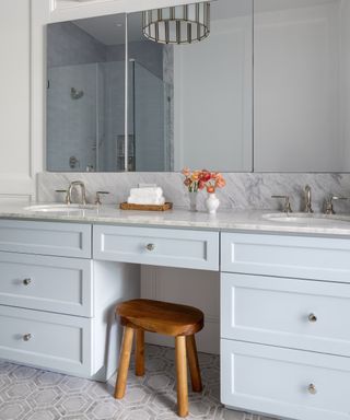 Double bathroom vanity in pale blue with wood stool and triple mirror, gray patterned floor and gray marble counter and backsplash