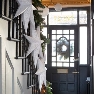 A hallway with a staircase with the railing decorated with a Christmas garland and star-shaped paper lanterns from IKEA