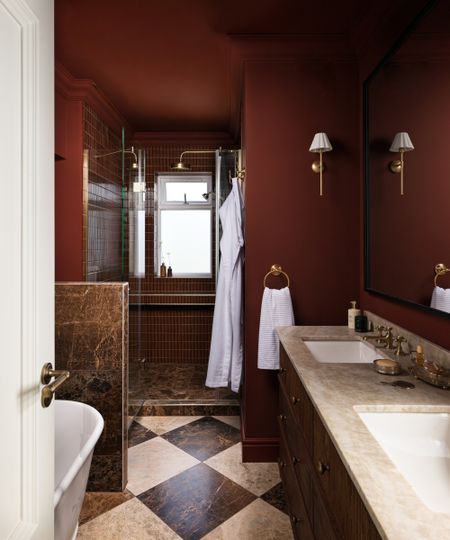 A moody bathroom color drenched in burgundy paint with burgundy marble tiles around the shower and bath