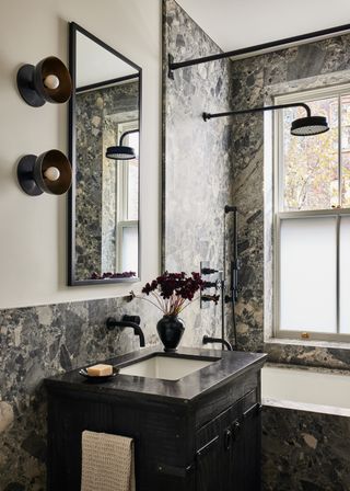 A dramatic dark stone bathroom featuring wall light fittings and stone covered walls