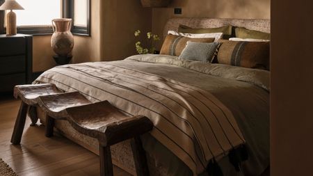 Cozy bedroom with double bed with mismatched bedding and white striped blanket, and wooden bench at the end of the bed.
