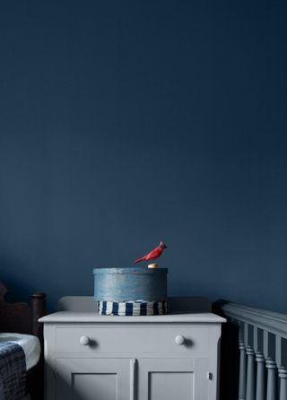 A bedroom with a gray nightstand and walls painted a dark inky blue