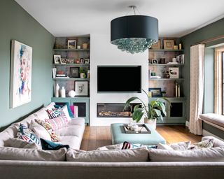 A green living room with large corner sofa, TV and floor to ceiling book shelves