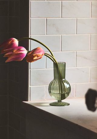 green tinted glass vase on a windowsill holding a couple of fresh blooms