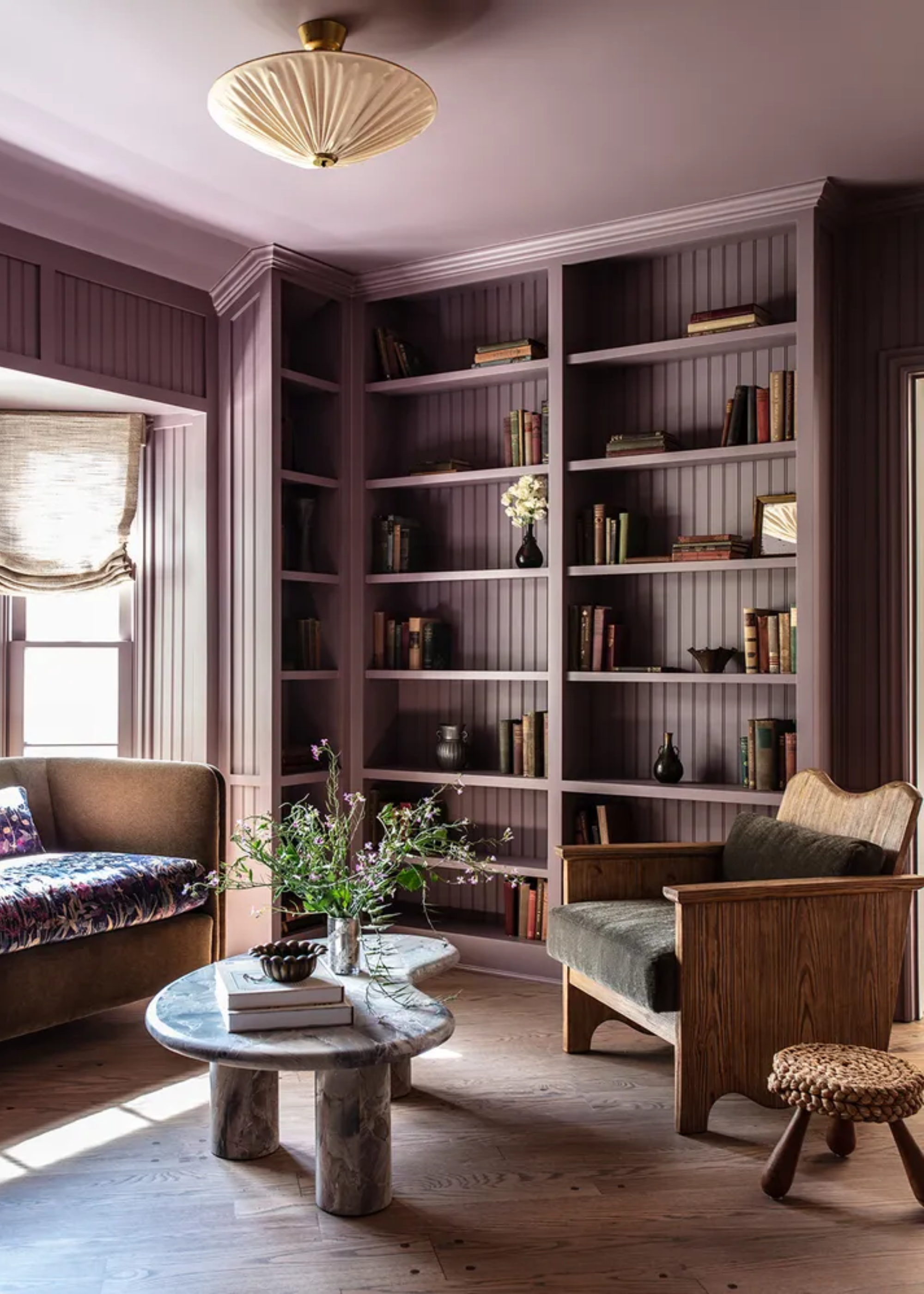 A purple reading room with a stone coffee table, a wood armchair, and a purple shelf of books