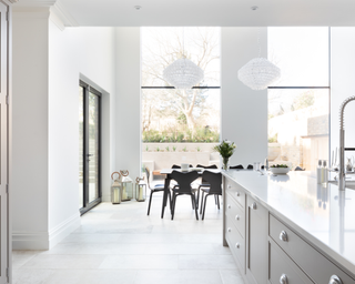 A minimalist white open plan kitchen idea with large windows and black chairs.