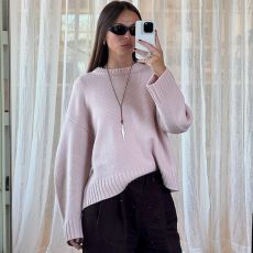 Scandinavian fashion creative Johanna Lager poses for a mirror selfie wearing black sunglasses, a chunky pink crewneck sweater, a red cord necklace with a silver fish pendant, and black pants