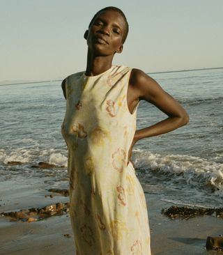 seorang model mengenakan gaun bermotif bunga kuning tanpa lengan di pantai