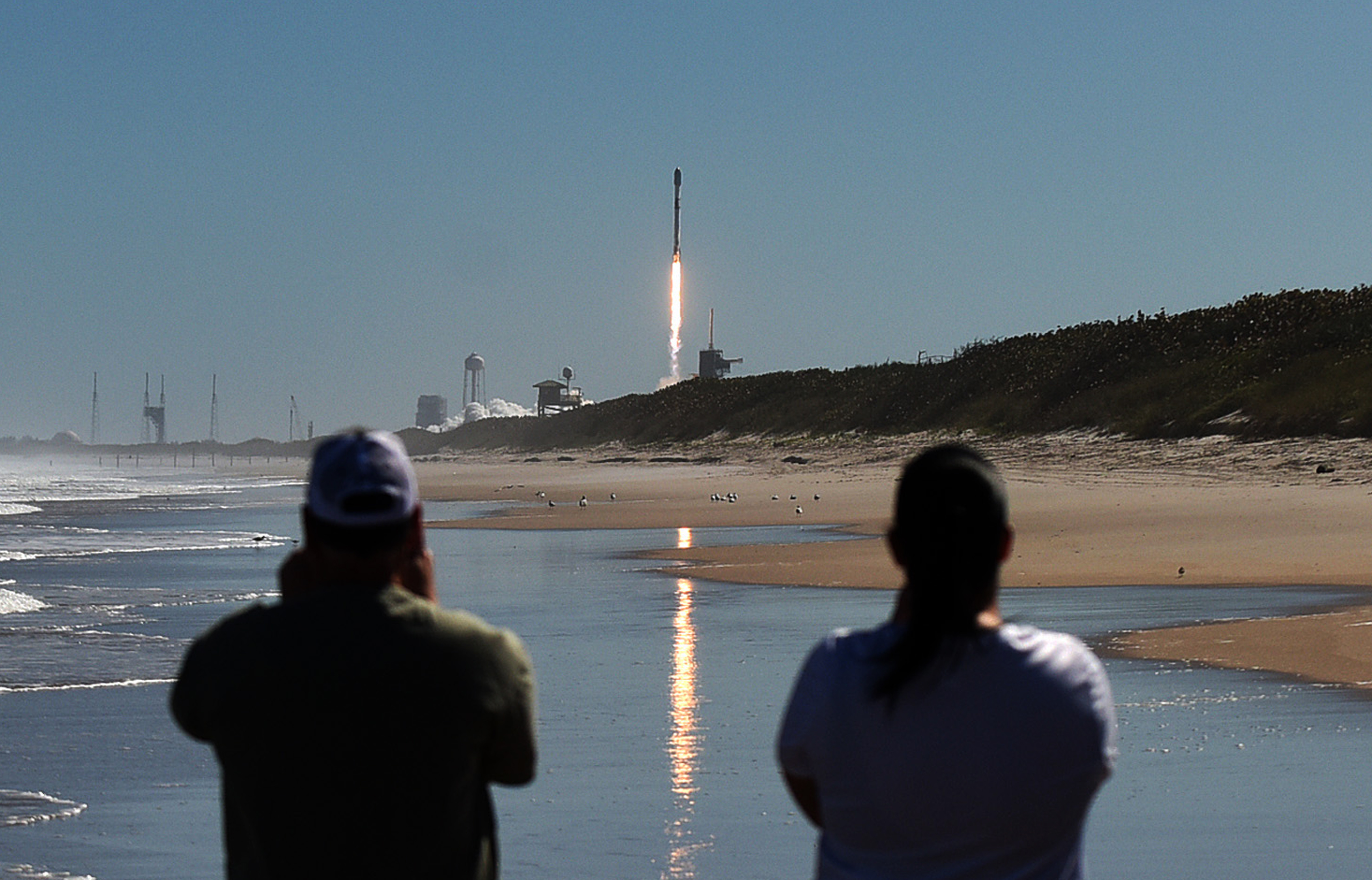People watch from Canaveral National Seashore as a SpaceX Falcon 9 rocket launches from pad 39A at the Kennedy Space Center in Cape Canaveral, Florida. The rocket is carrying 49 Starlink internet satellites for a broadband network.
