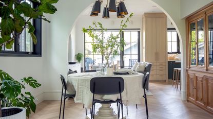 Modern dining room with round table, black chairs in center of room with wooden hutch visible to the right and lots of house plants