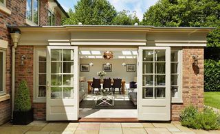 a Westbury orangery with sliding traditional doors - with a lounge space near the doors and a wooden dining table beyond