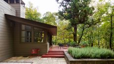 Midcentury house with panelled exterior, red steps and outside table and chairs amongst trees