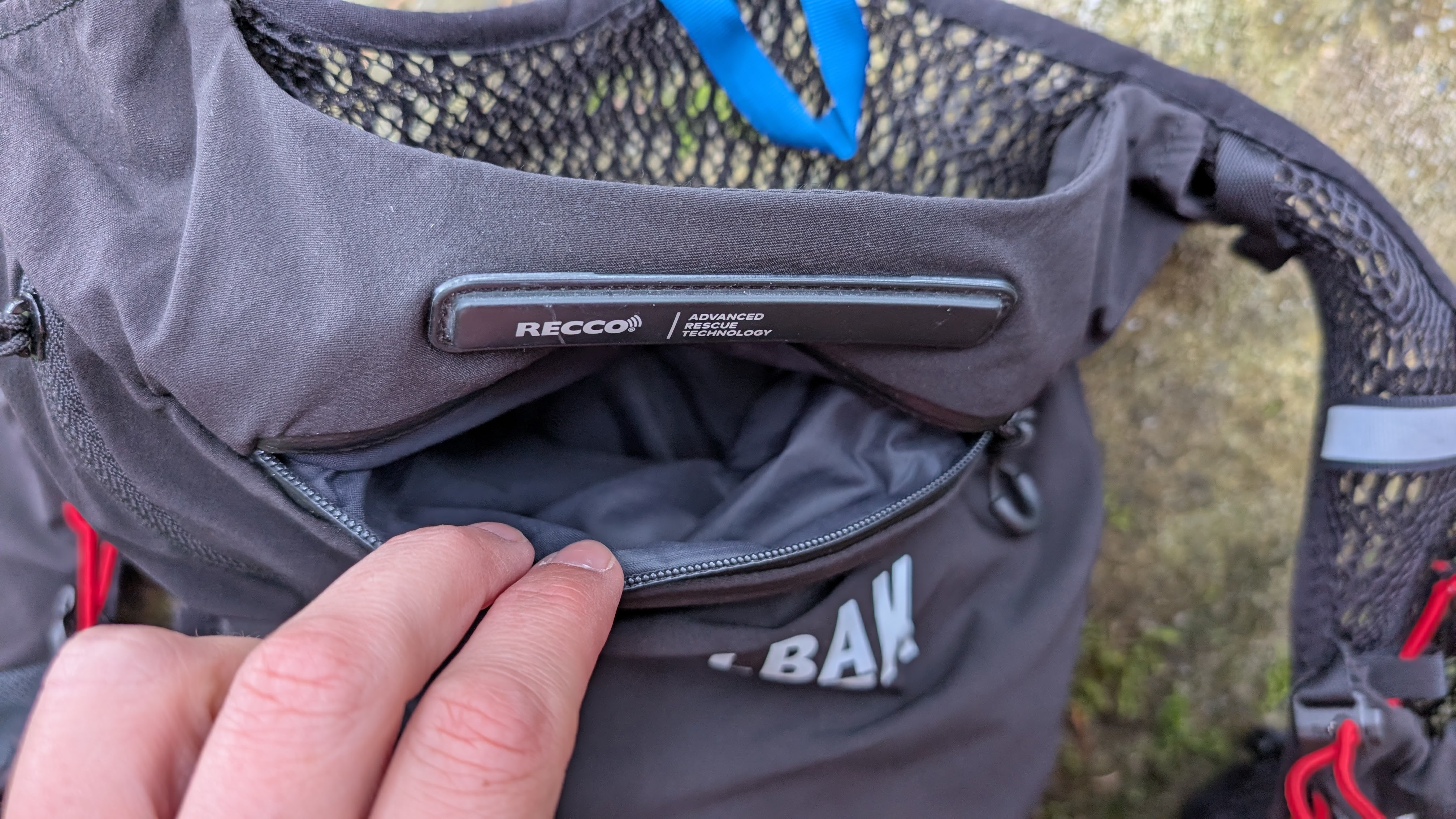 A runner's hand shows the waterproof pocket at Recco reflector on a black Camelbak Apex Pro running vest