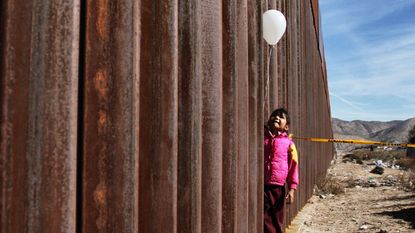 A little girl holds a white ballon at the border wall between Mexico and the United States