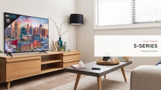 TCL 5-Series 4K TV in a living room on a TV stand while displaying a city scape scene