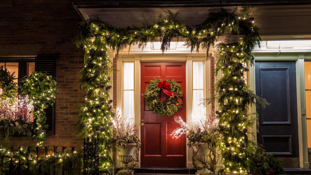 Christmas foliage surrounding a red door with pine cones and fairy lights