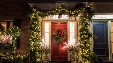 Christmas foliage surrounding a red door with pine cones and fairy lights