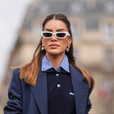 Camila Coelho wears white sunglasses, earrings, a navy blue oversized blazer jacket, a polo shirt, a checkered / checked pattern printed shirt, a white mini skirt , a leather bag, outside Miu Miu , during the Womenswear Fall/Winter 2024/2025 as part of Paris Fashion Week on March 05, 2024 in Paris, France