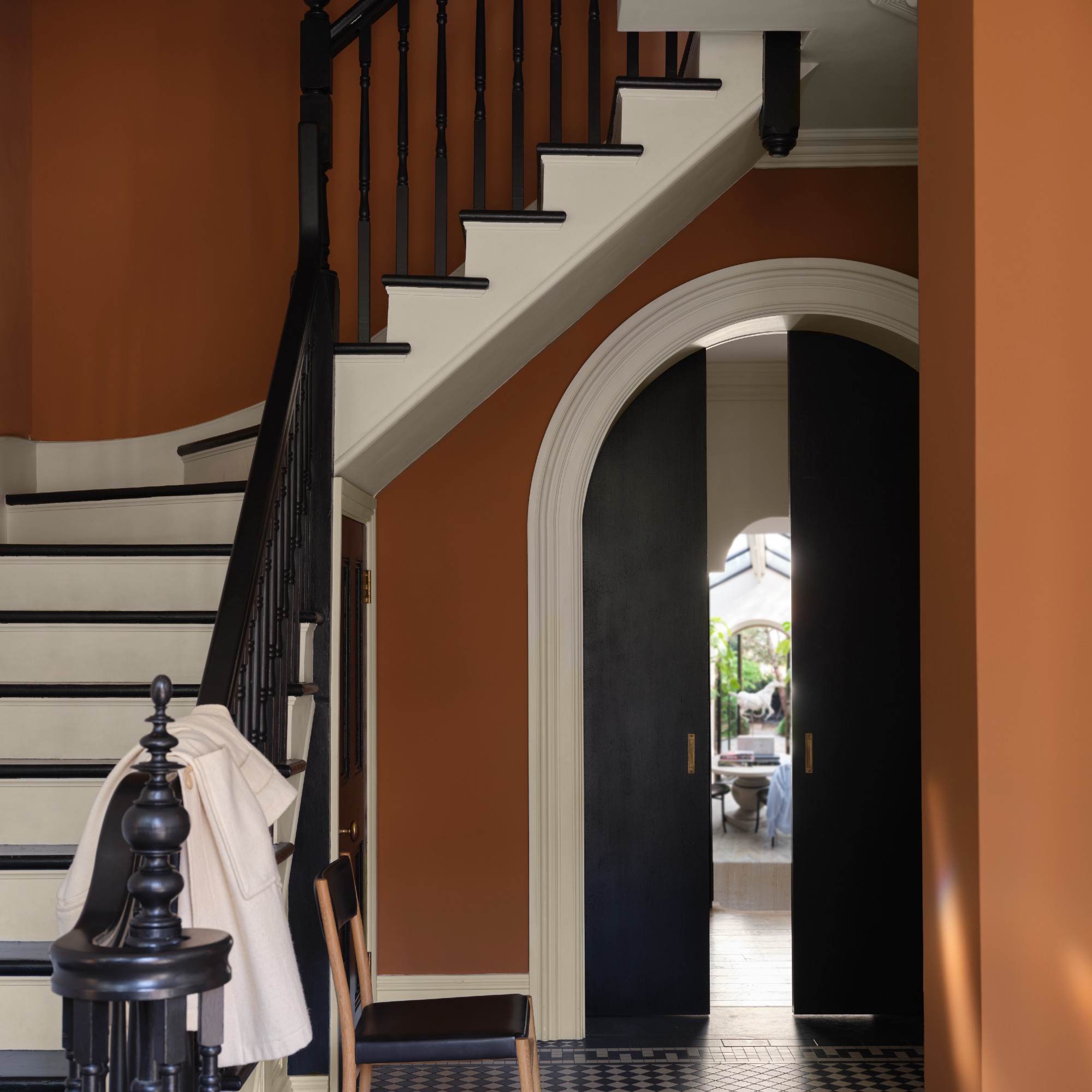 A hallway painted in Farrow &amp;amp; Ball&#039;s Marmelo shade with a winding staircase and arched charcoal black doors