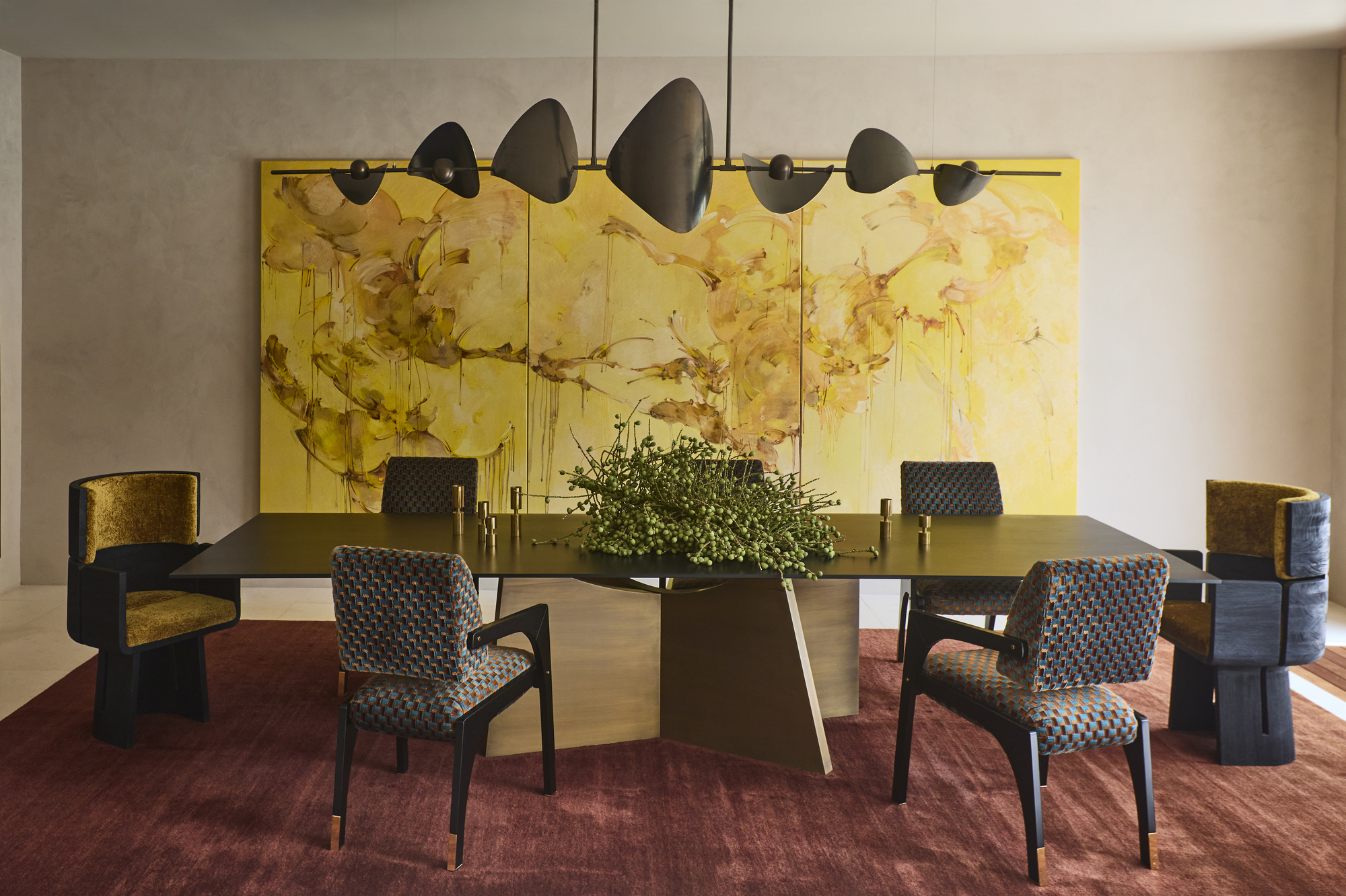 formal dining room with limewash walls, a long dining table with fabric upholstered dining chairs, a large red rug, a floral display in the middle of the table, a large yellow artwork on the wall and a sculptural pendant light suspended above the table