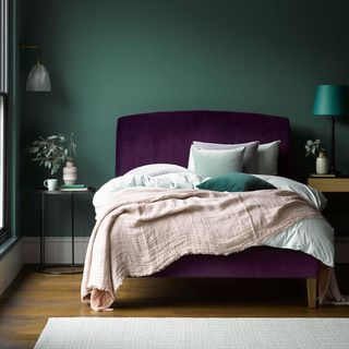 A bed with purple headboard, white bedding and a pink throw