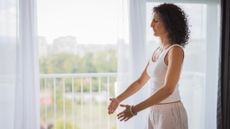 Woman standing in front of open window with her eyes closed and her hands held in front of her