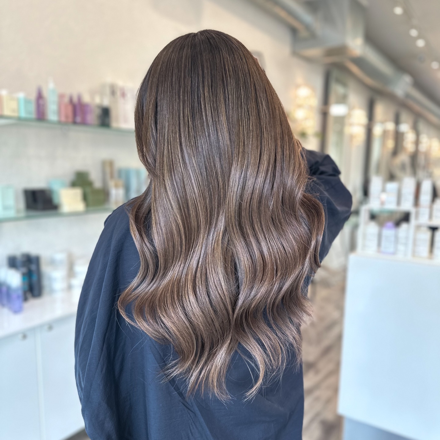 a person at the hair salon in the black salon cape and long brown hair