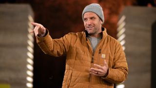 TJ Lavin in a brown coat hosting The Challenge: USA season 2