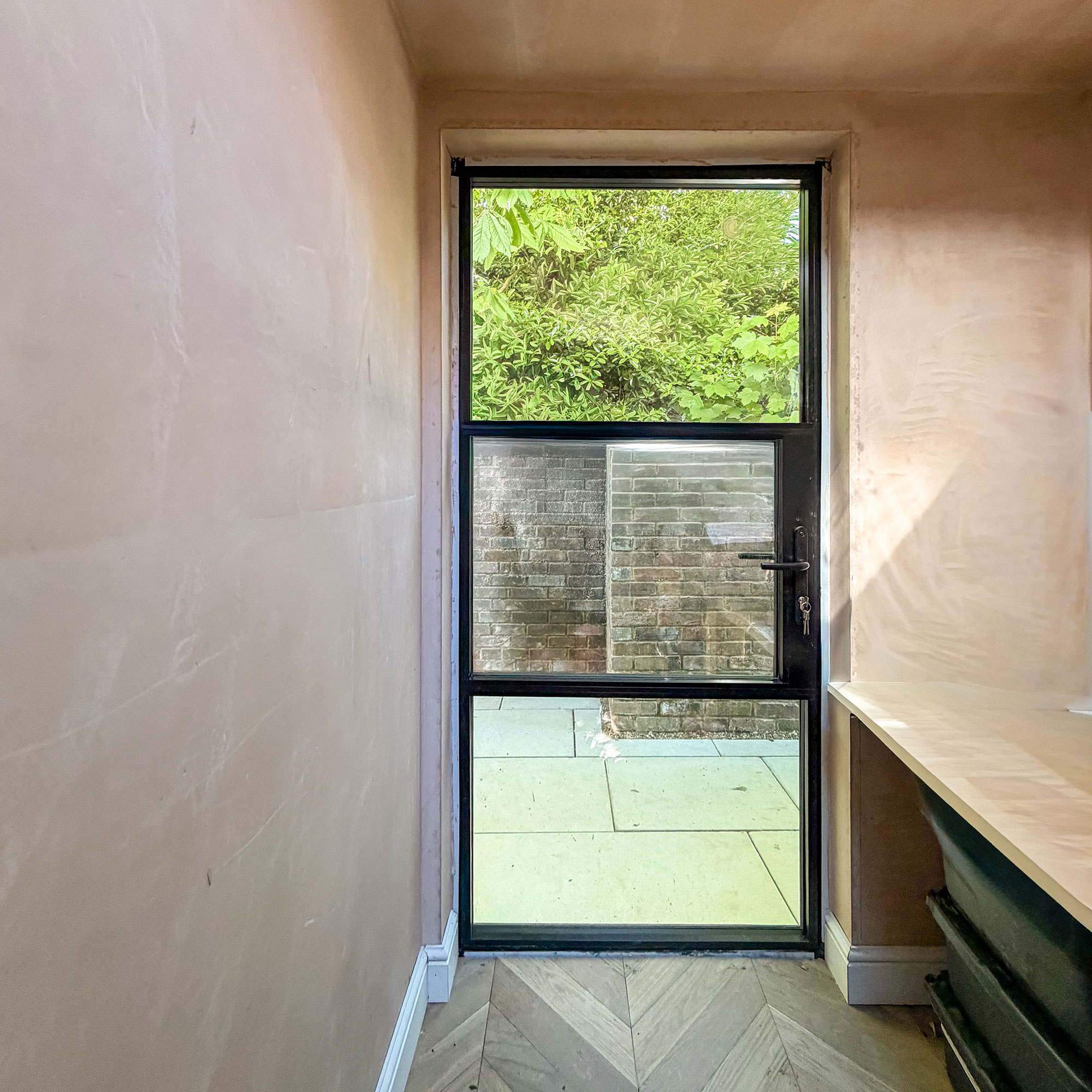 Room mid-renovation with plaster walls, wooden parquet and Crittal style door looking out onto paved patio