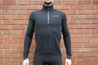 A rider wearing the Le Col Pro Rain Jacket in an all-black colorway