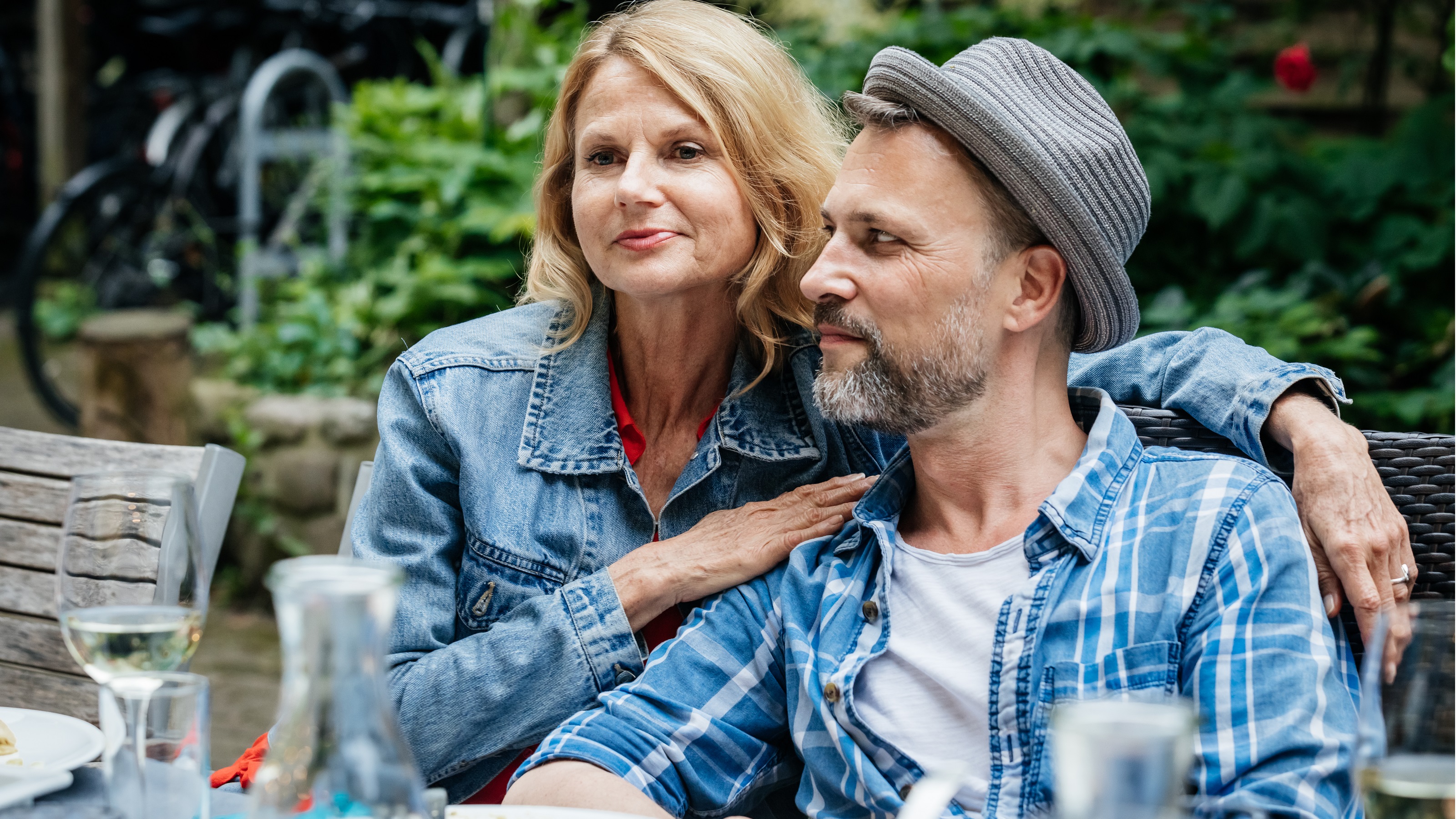 A fiftysomething couple sit very close together while dining outside. 