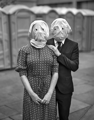 two people looking at the camera wearing pillowcases on their heads with eye holes cut out