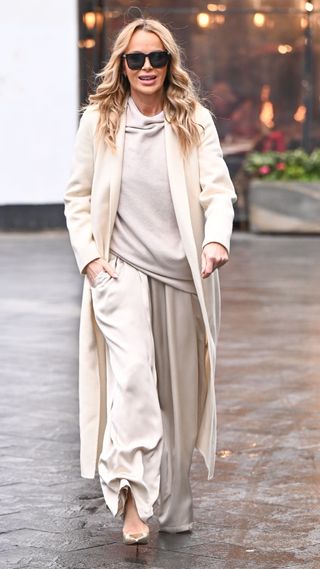 Amanda Holden wearing satin wide leg trousers, white knit jumpers, trench coat and metallic heels on January 23, 2025 in London