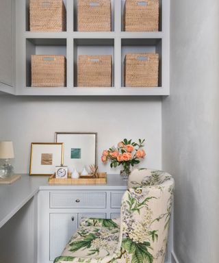 small home office painted in a light blue grey with a small floral upholstered desk chair and built in shelving, storage, and desk