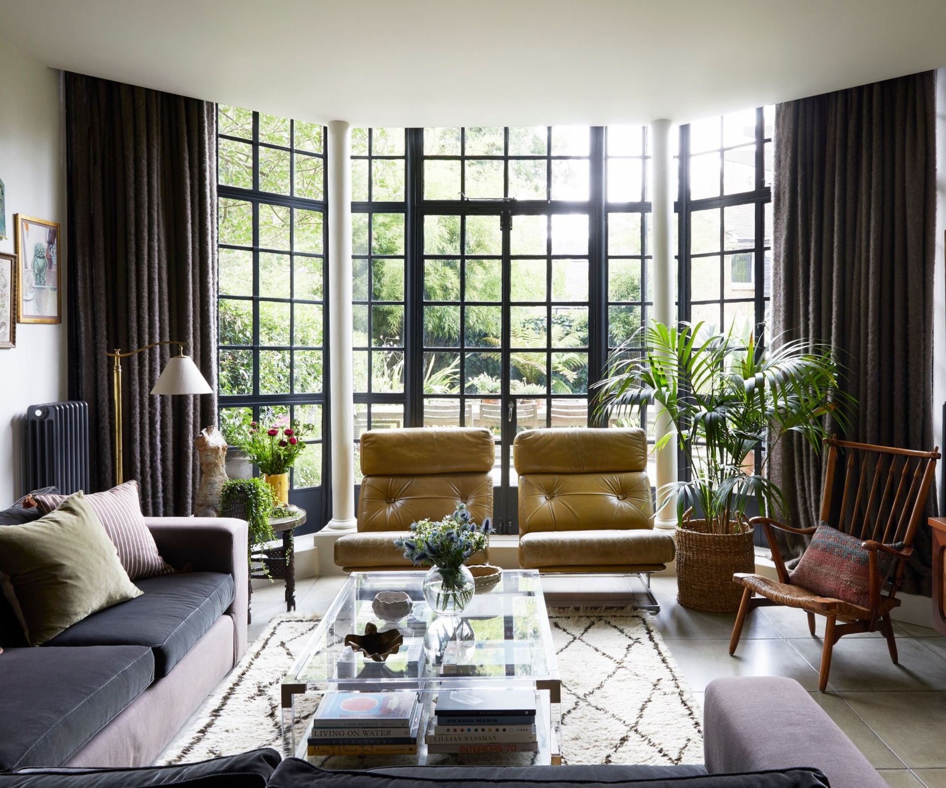 Living room with large crittal windows, two leather yellow armchairs, velvet purple sofa and glass coffee table
