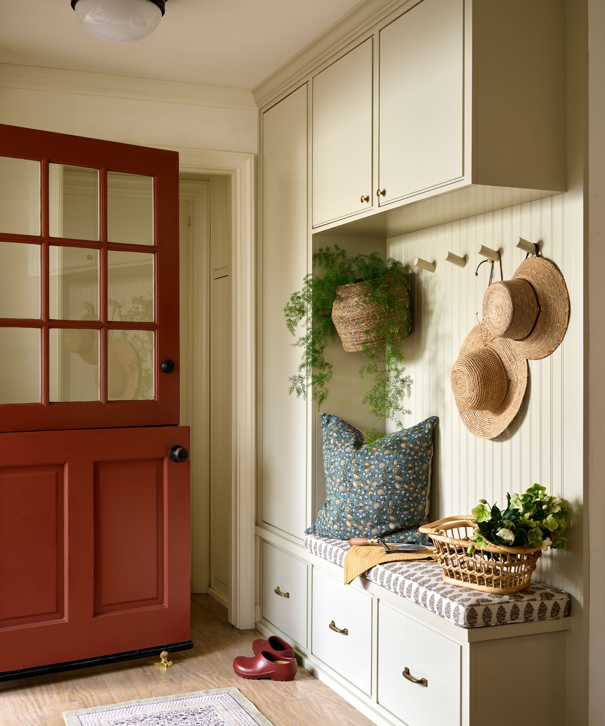 a warm soft yellow entryway with red dutch door and mudroom storage