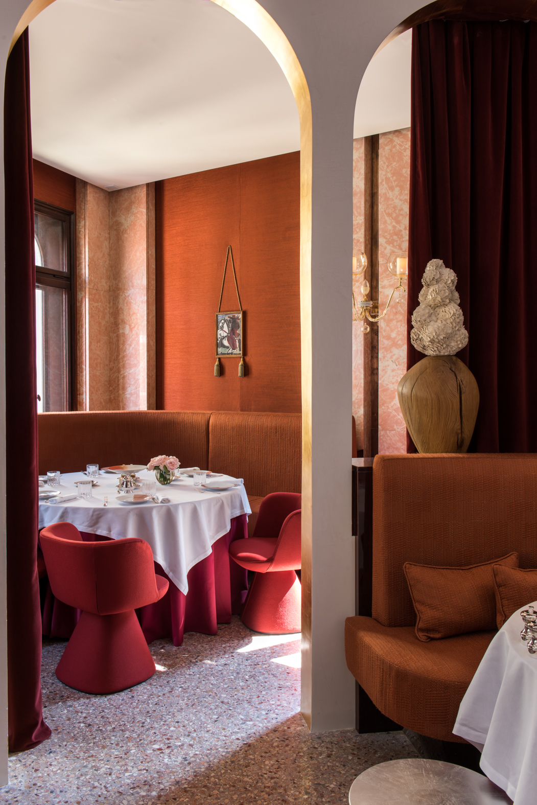 An inventively designed hotel restaurant mixes traditional and contemporary decor accents, including Space Age red chairs, terrazzo floors, sumptuous textile banquettes, and marble detailing.