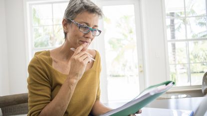 An older woman looks over paperwork, looking like she's contemplating something.