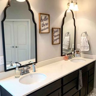 bathroom with white walls black cabinet with wash basin with large mirror on wall and towel and images