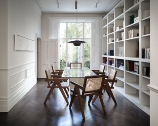 Modern dining room ideas with white walls and bookshelf wall, French windows and a long table with rattan-backed club chairs