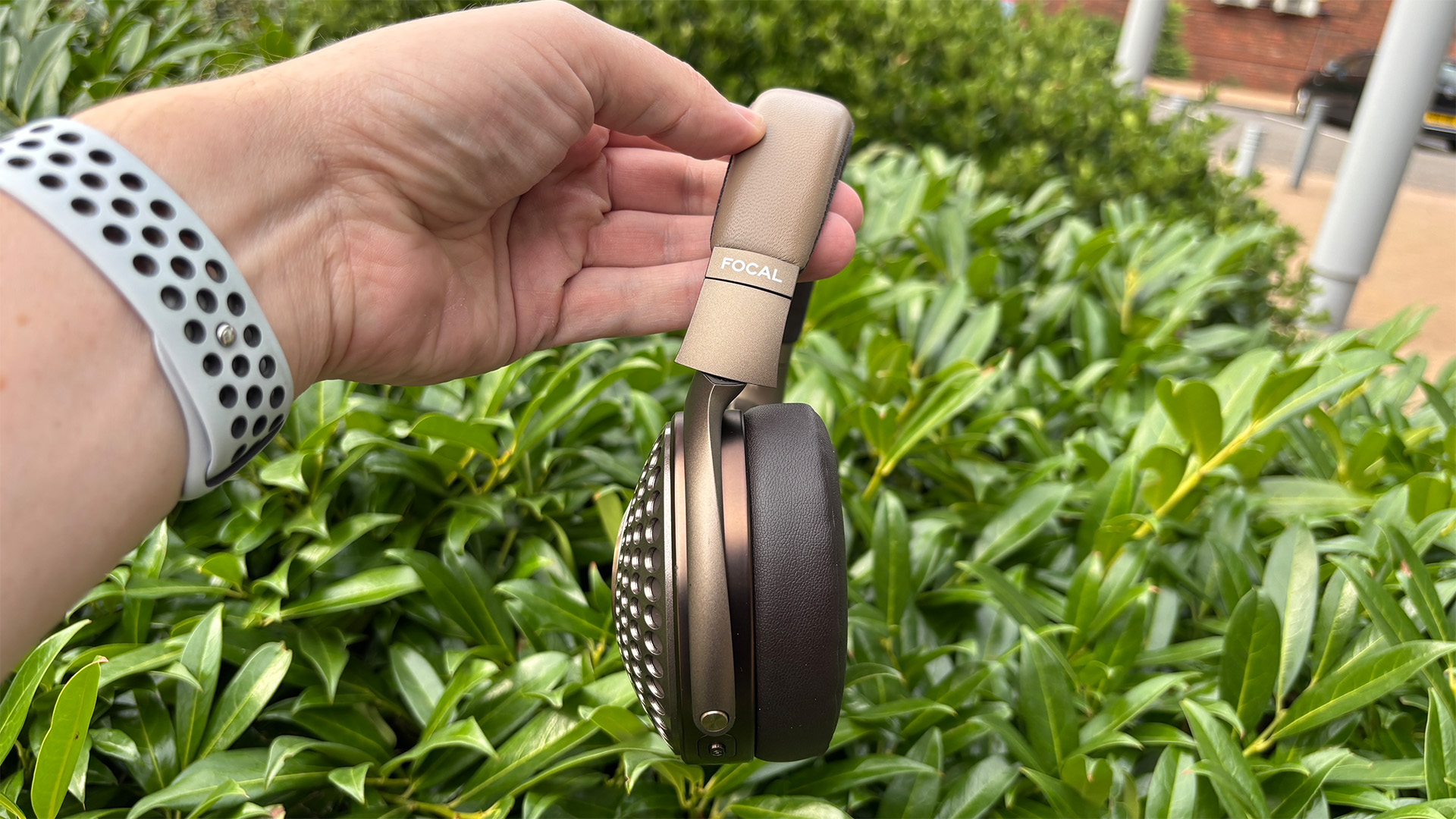 Focal Bathys MG wireless headphones held in hand in front of green bush
