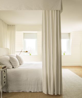 White bedroom with canopy, white linen bedding, white rug and wood bedside table