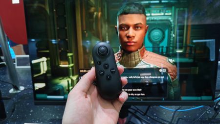 A reviewer holding the Acer Smart Dial in front of a gaming monitor that's playing Outer Worlds 2