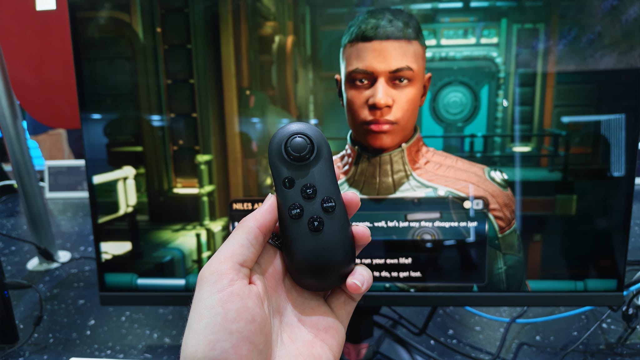 A reviewer holding the Acer Smart Dial in front of a gaming monitor that's playing Outer Worlds 2