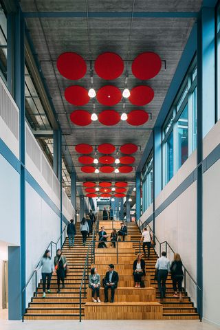 Wooden staircase with red acoustic baffles and white walls with blue details. captured with people walking up and down the stairs