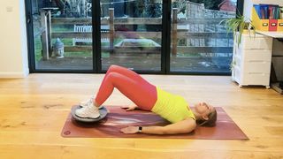 Woman performs a glute bridge with her feet on a wobble board