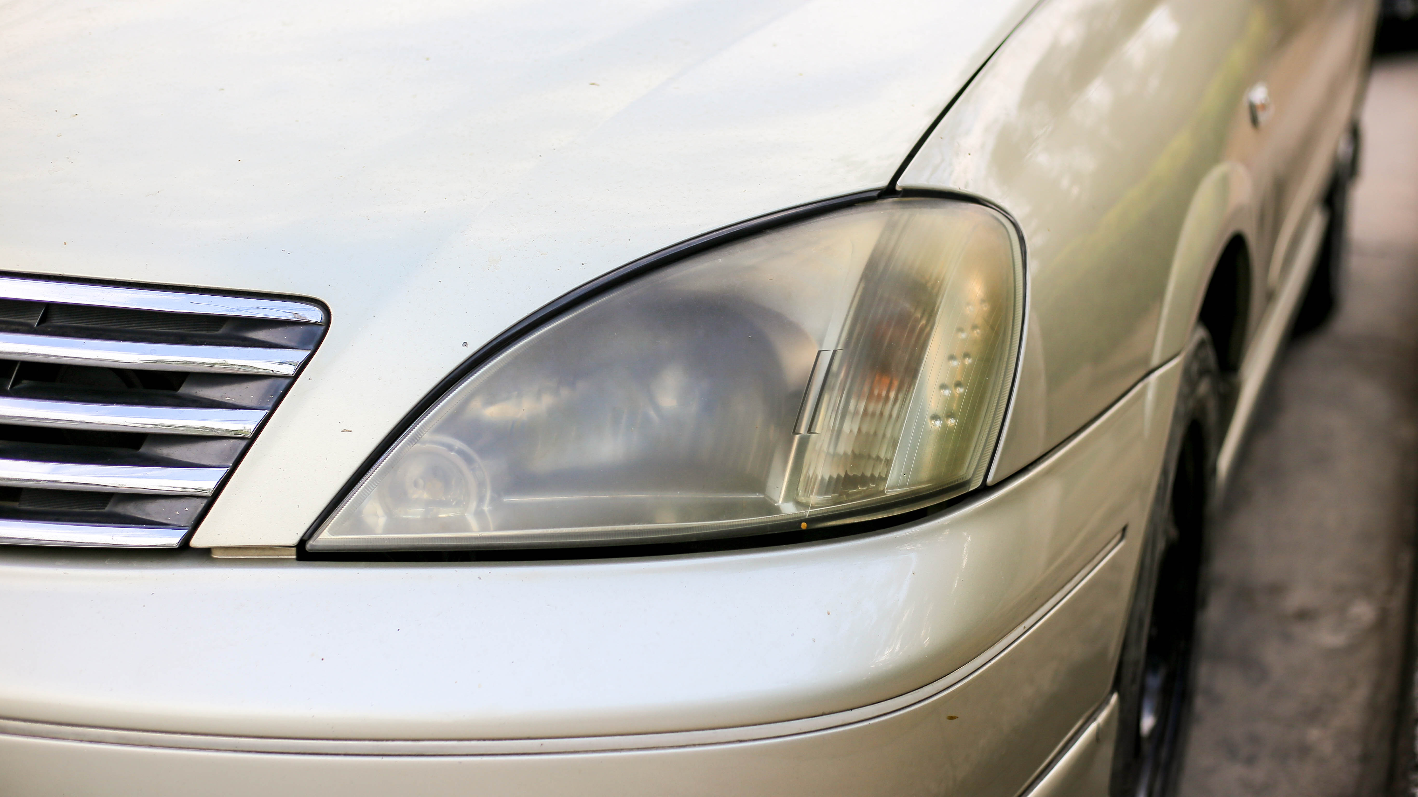 Headlights on a silver car which are foggy and have yellowed