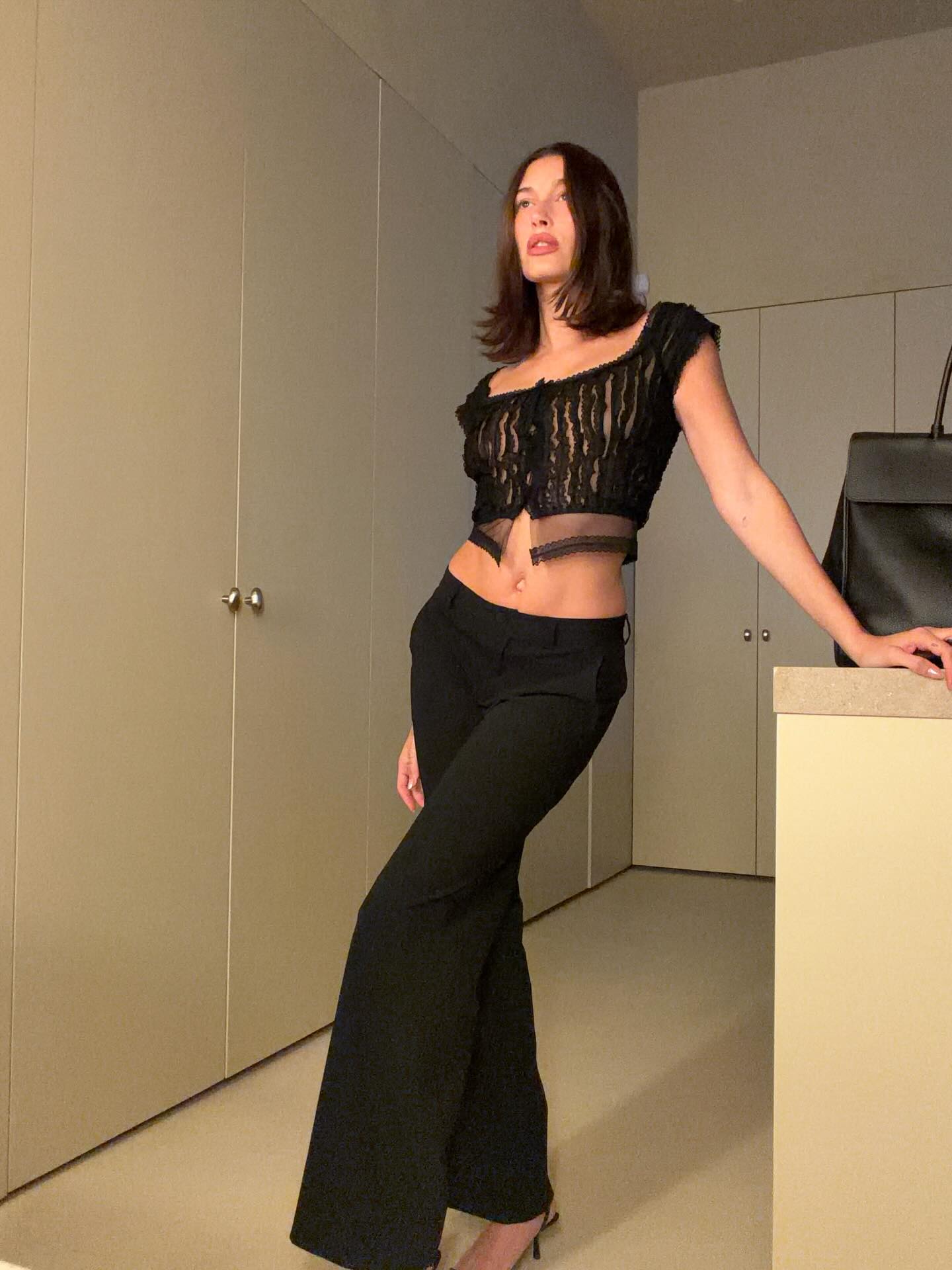 Hailey wears a cropped black top with low-rise black pants.