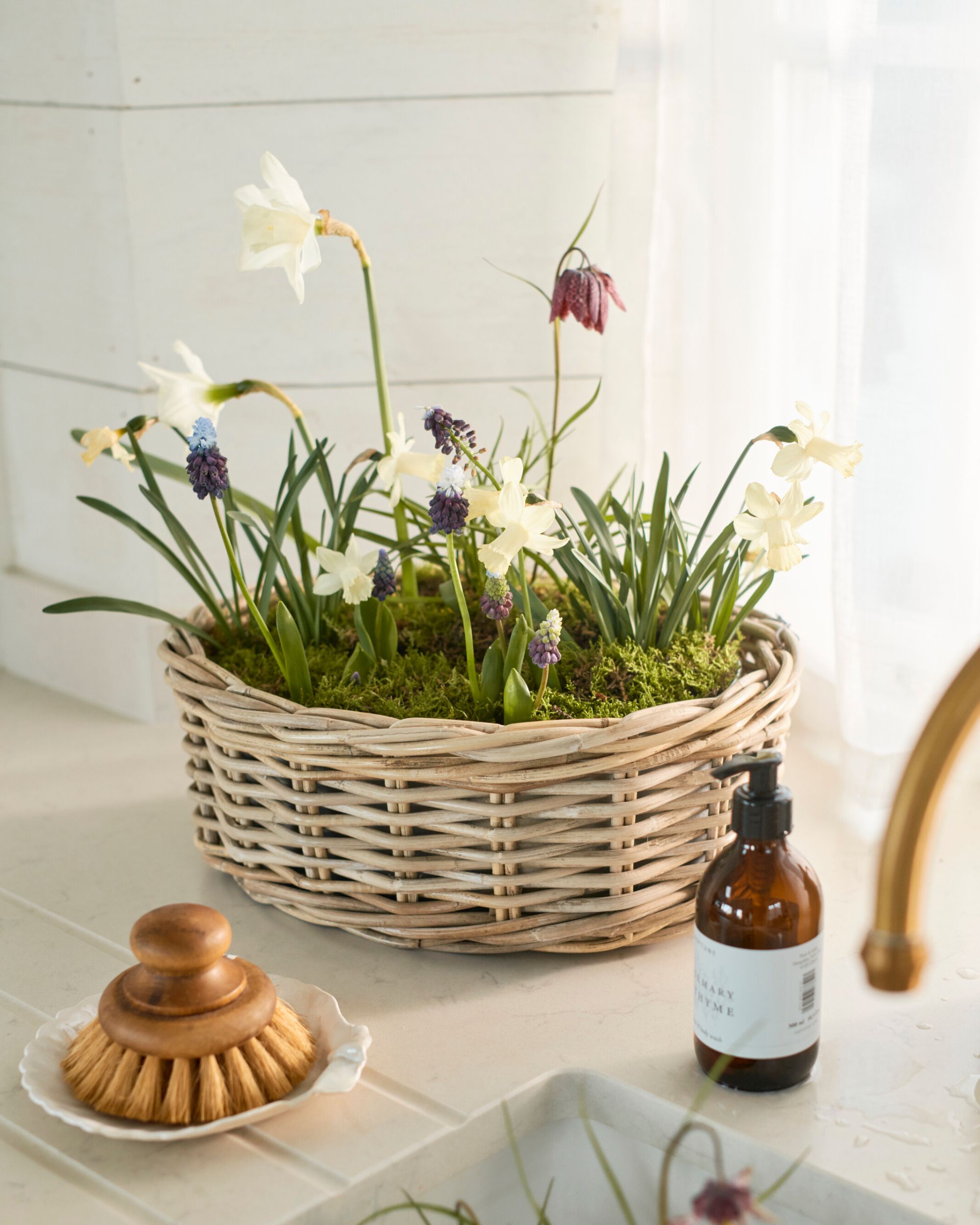 A small wicker planter with spring flowers planted by a sink.